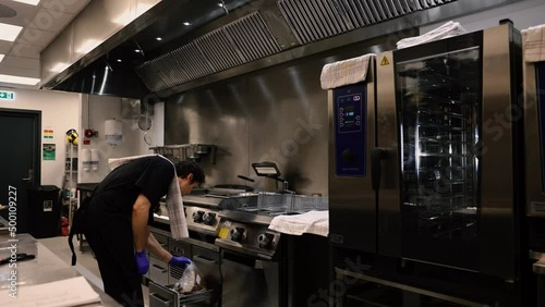 Professional chef in the kitchen of a restaurant. A male chef in a black uniform is working in the kitchen. Slow motion 4K