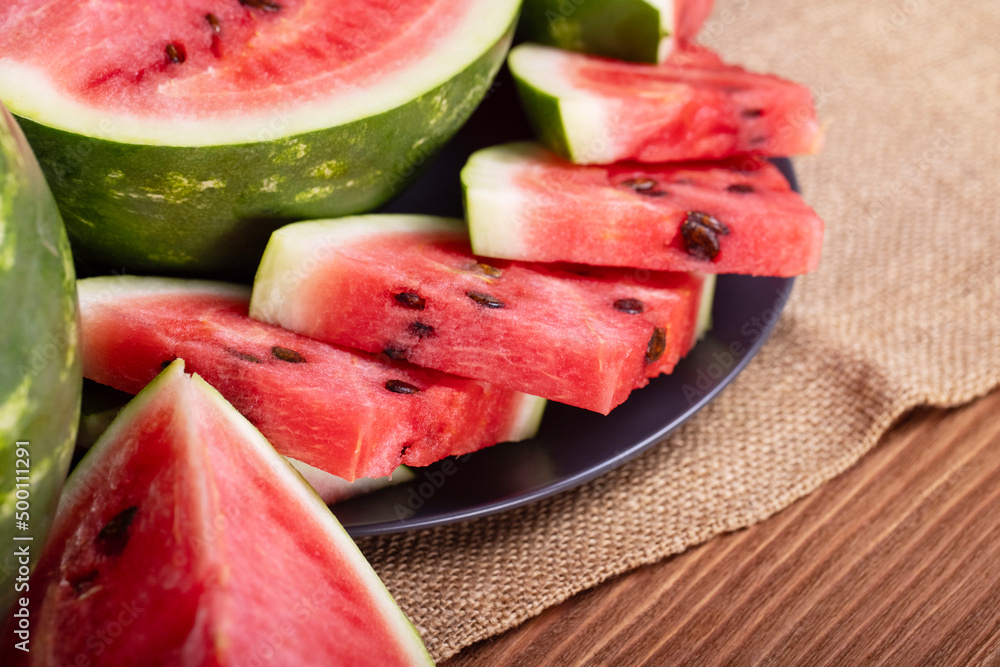 Fresh red watermelon pieces on a black plate on a wooden table. Sweet and juicy watermelon Fresh red watermelon pieces on a black plate on a wooden table. Sweet and juicy watermelon