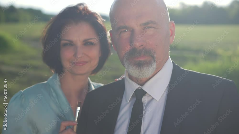 Portrait of talented confident elegant man looking at camera standing in sunlight with happy woman. Handsome Caucasian husband posing in slow motion with smiling wife holding painting brush Portrait of talented confident elegant man looking at camera standing in sunlight with happy woman. Handsome Caucasian husband posing in slow motion with smiling wife holding painting brush