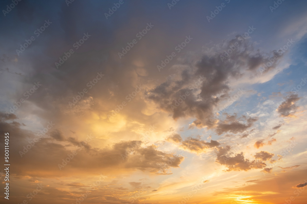 Dramatic sunset landscape picture with puffy clouds lit by orange setting sun and blue sky