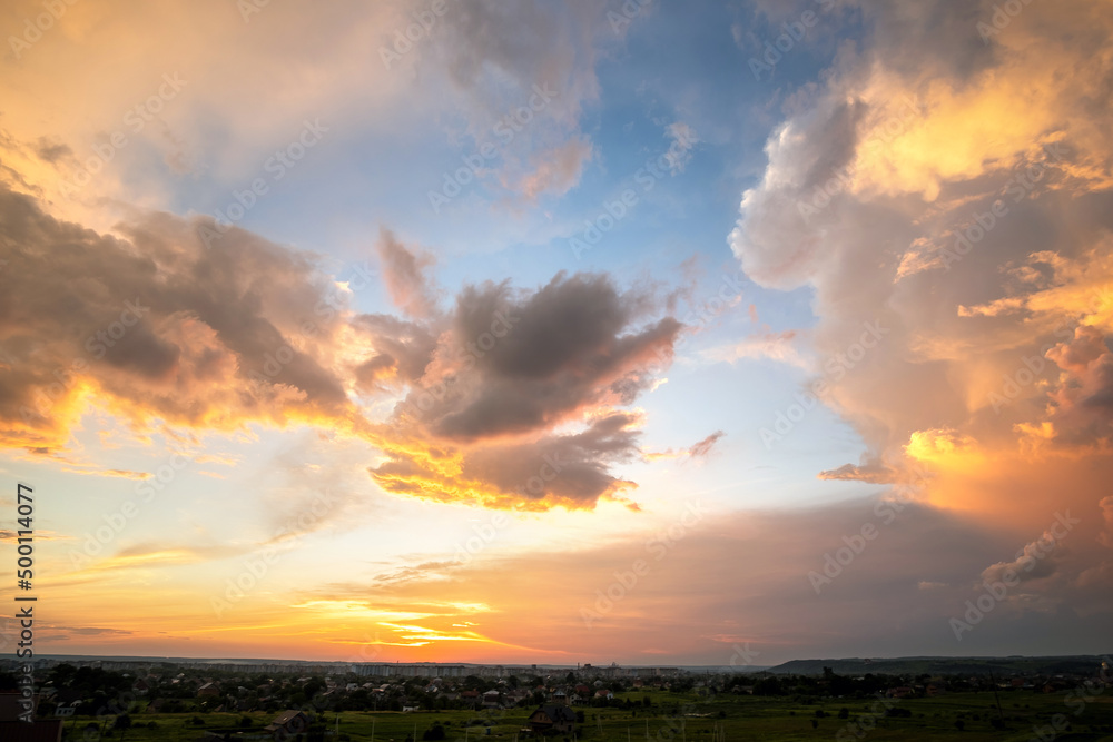 Obraz premium Dramatic sunset landscape with puffy clouds lit by orange setting sun and blue sky.