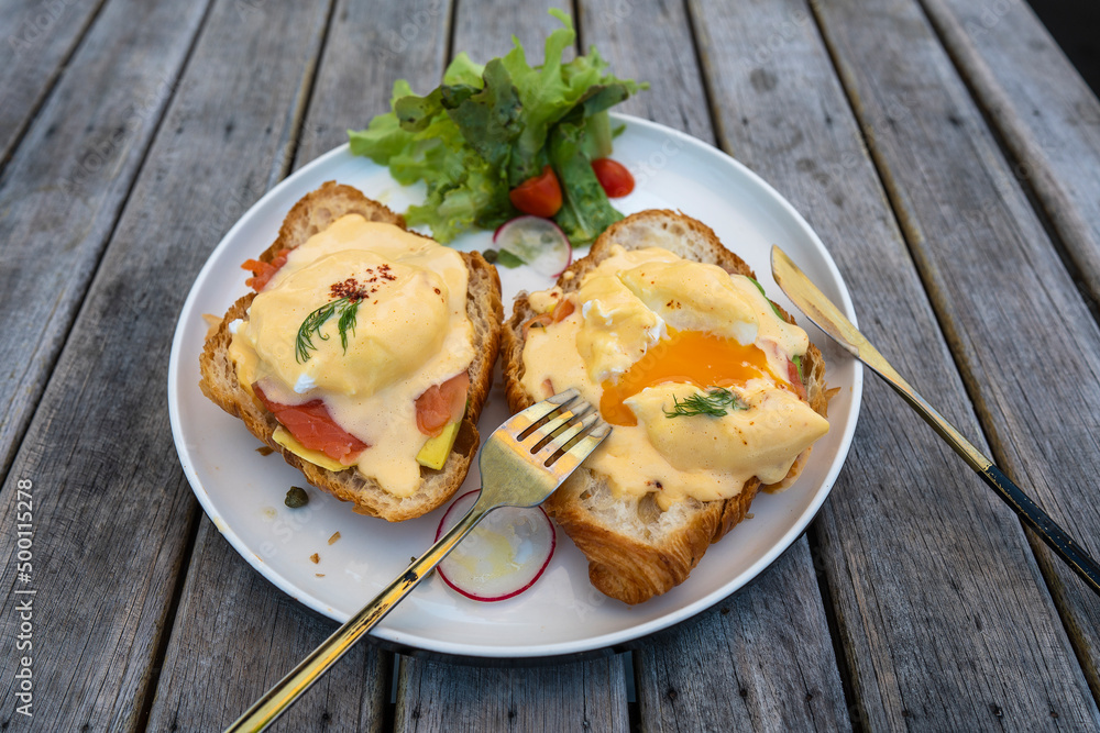 Croissant sandwich with poached egg, radish and salmon on plate in cafe Croissant sandwich with poached egg, radish and salmon on plate in cafe