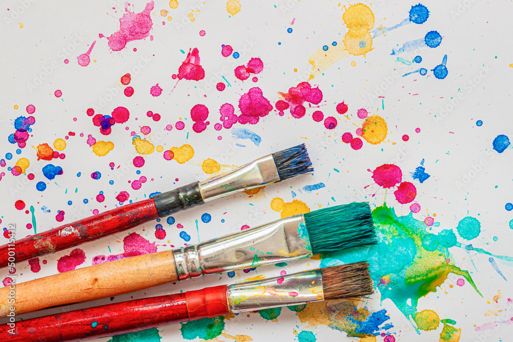 Artist paint brushes on background of colorful watercolor splashes, vivid blots