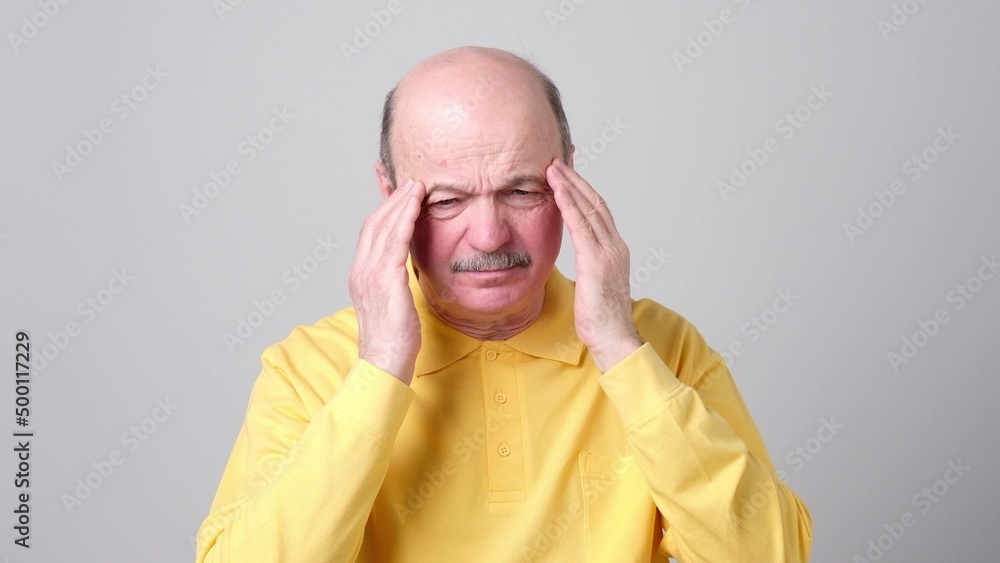 Mature man in yellow tshirt with closed eyes touching his head in pain. Mature man in yellow tshirt with closed eyes touching his head in pain.