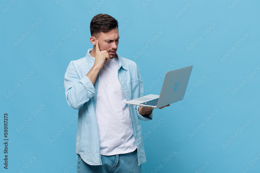 Thoughtful tanned handsome man in casual basic t-shirt concerned make difficult decision with laptop posing isolated on blue studio background. Copy space Banner Mockup. Electronics repair IT concept Thoughtful tanned handsome man in casual basic t-shirt concerned make difficult decision with laptop posing isolated on blue studio background. Copy space Banner Mockup. Electronics repair IT concept