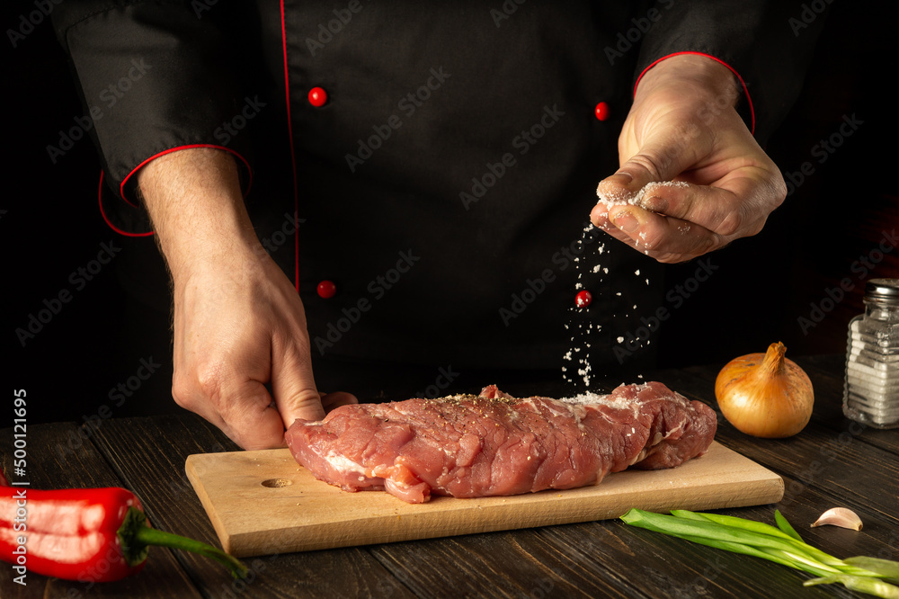 Beef must be salted before cooking. The chef is salting raw veal in the kitchen. Asian cuisine. Recipe idea for a hotel