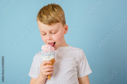 Positive boy licking ice cream on a blue background. Health benefits ice cream concept. 