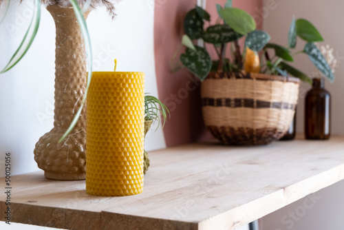 A textured beeswax pillar candle is displayed on a shelf with various decor.