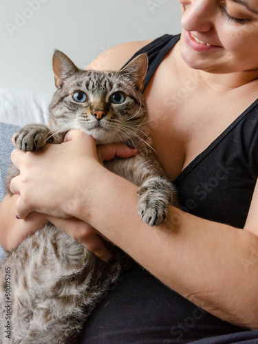 happy woman holding a cat indoors, sitting on a couch 