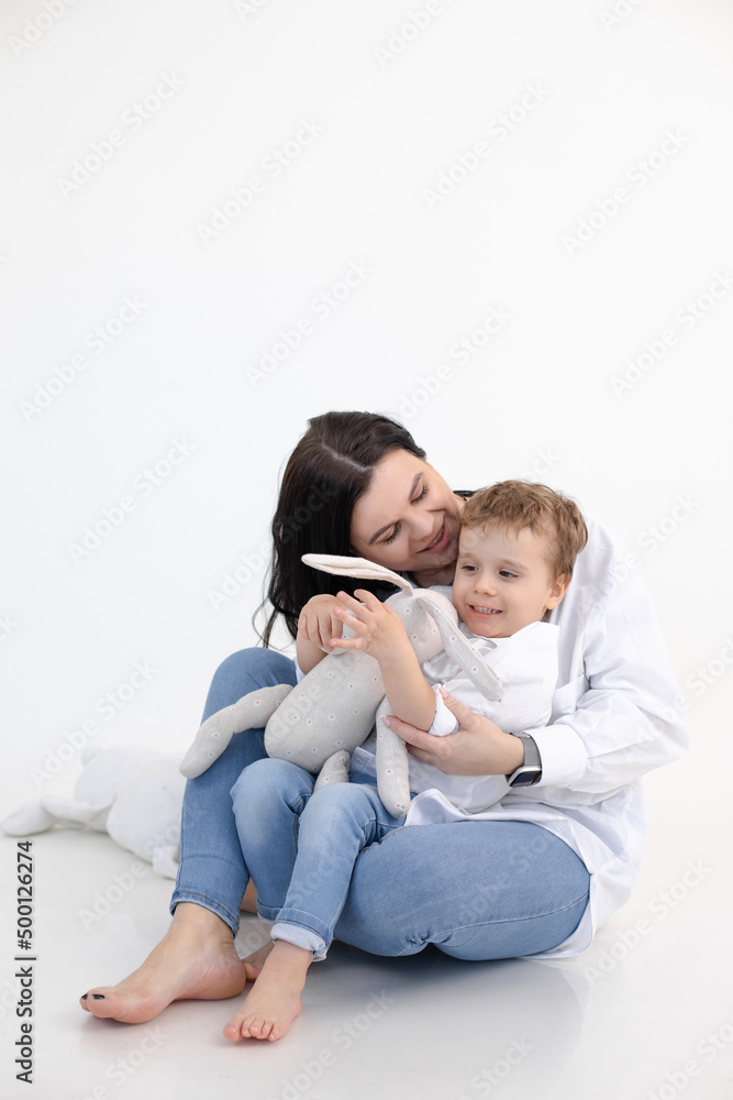 Vertical photo of barefoot woman playing with son, hold soft toy rabbit. Kid development, playing together. Happy family