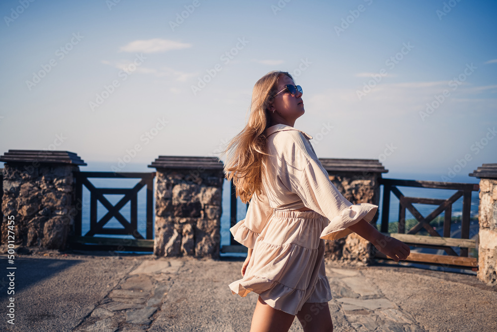 A young woman with long blond hair in a top and a skirt is walking on a summer sunny day. Happy girl with a smile on her face and in sunglasses is walking on a sunny day