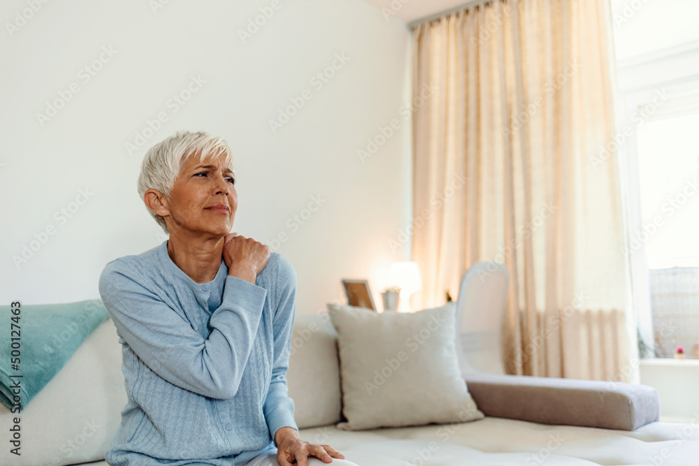Stressed mature woman massaging her neck. Mature woman suffering from neck pain at home. Portrait of elderly woman having a neck pain in the living room. Stress and depression. Stressed mature woman massaging her neck. Mature woman suffering from neck pain at home. Portrait of elderly woman having a neck pain in the living room. Stress and depression.