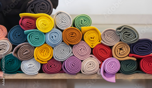 Multi-colored knitted fabrics rolled up in rolls lying on shelf of store, factory