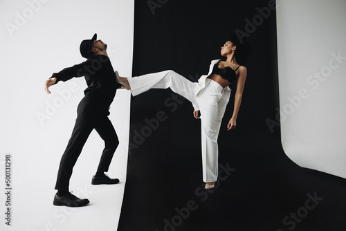 European man in black suit on a white background dancing with young african american woman with curly hair on a black background