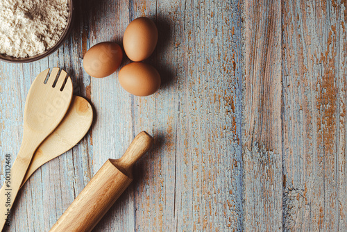 overhead shot on weathered wooden work table with eggs, whisk, rolling pin, flour. Copy space on the right