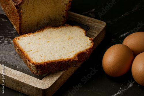 close up photo of sponge cake on wooden and stone board with fresh eggs on black marble background photo