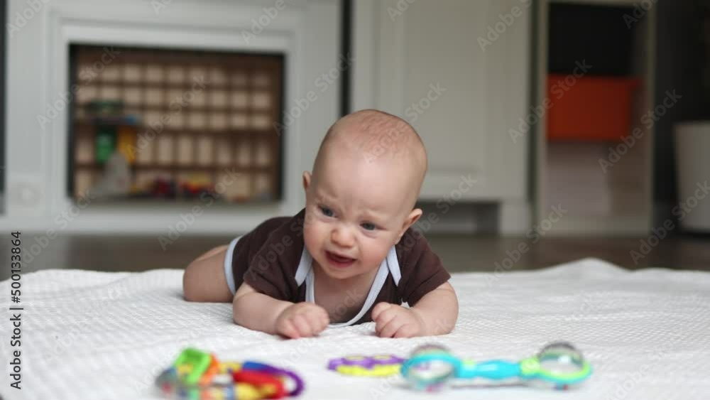 little baby infant learning to crawl on the floor in living room, child kid trying to reach colorful toys, lying on tummy on white blanket indoors. physical education training for babies activities little baby infant learning to crawl on the floor in living room, child kid trying to reach colorful toys, lying on tummy on white blanket indoors. physical education training for babies activities