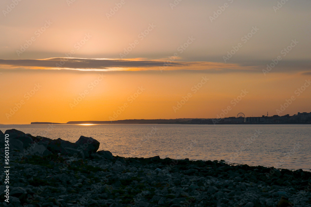 Galway bay at sunset. Silhouette of Salthill area. Dark and moody feel. Warm orange color. Nature scene. Irish landscape.