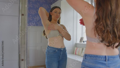 Woman in underwear self examining breast for signs of lumps or cancer symptoms at home in mirror - shot in slow motion