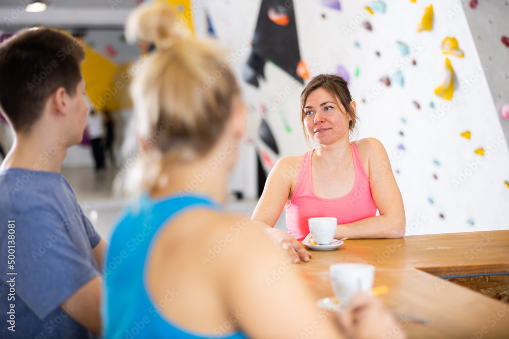 Two sports women and a guy communicate after training on a climbing wall at a table in a cafe