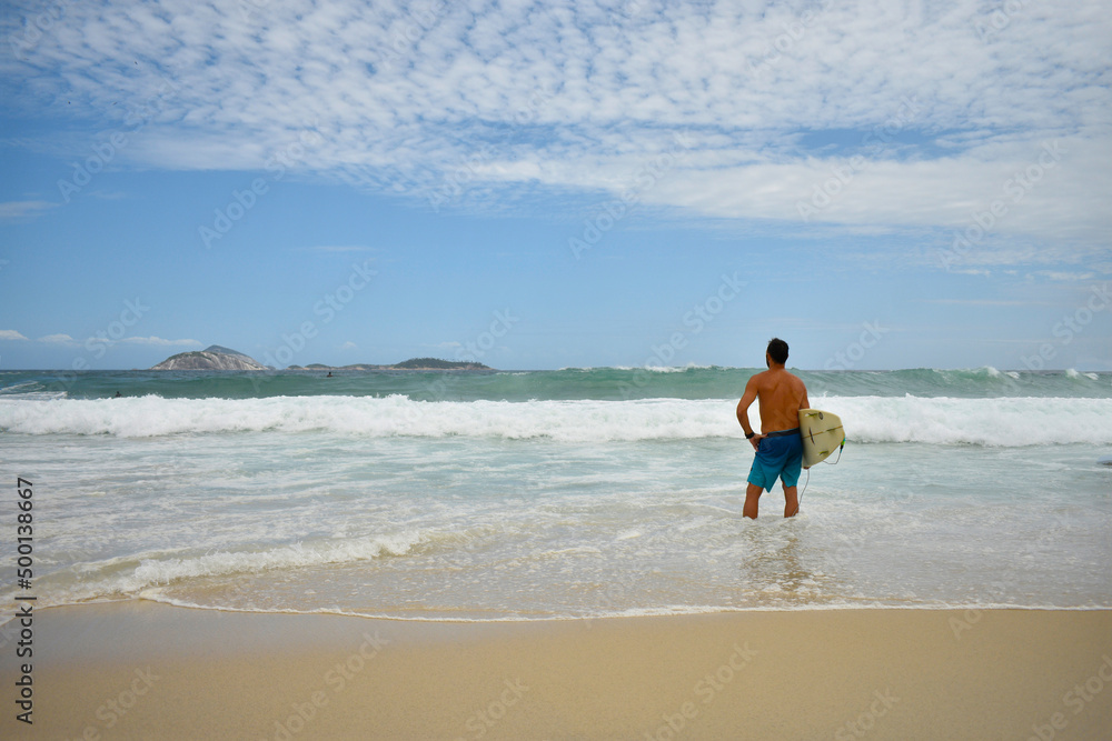 surfer looking at the green sea and its waves under a clear blue sky on a beautiful lonely beach surfer looking at the green sea and its waves under a clear blue sky on a beautiful lonely beach