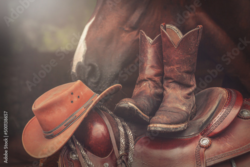 Cowboy hat and worn leather boots on western saddle with horse in background