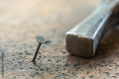 Funny close-up of nails with smiley faces on it and a hammer in the background on a wooden table in a workshop
