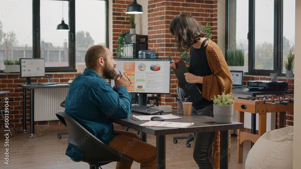 Business man asking for help from woman to design rate charts on computer monitor. Entrepreneur and colleagues doing teamwork to plan data analysis on display for startup presentation. Business man asking for help from woman to design rate charts on computer monitor. Entrepreneur and colleagues doing teamwork to plan data analysis on display for startup presentation.