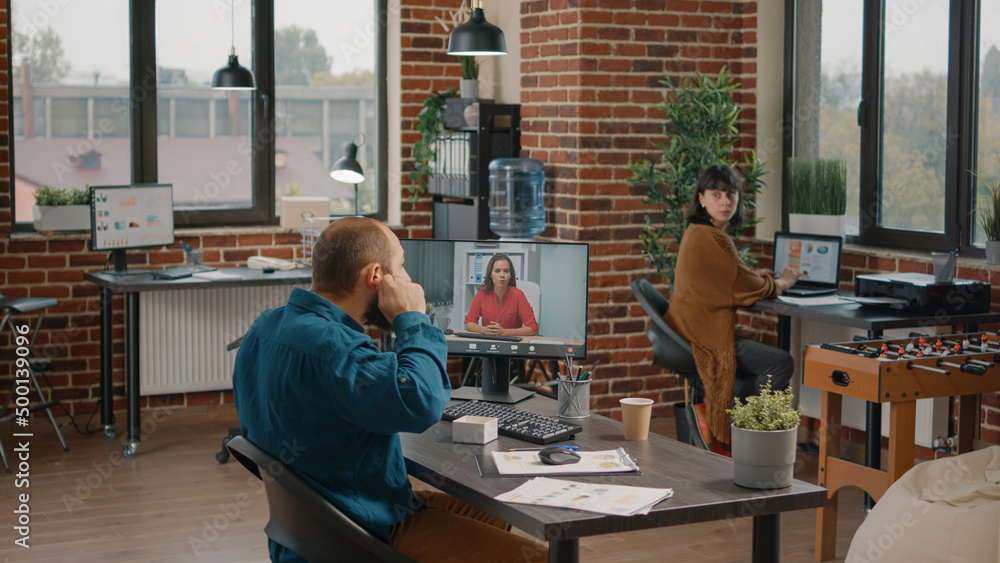 Entrepreneur using earpods to talk to manager on video call in startup office. Business man talking to woman on remote online video conference on computer to plan project and strategy. Entrepreneur using earpods to talk to manager on video call in startup office. Business man talking to woman on remote online video conference on computer to plan project and strategy.