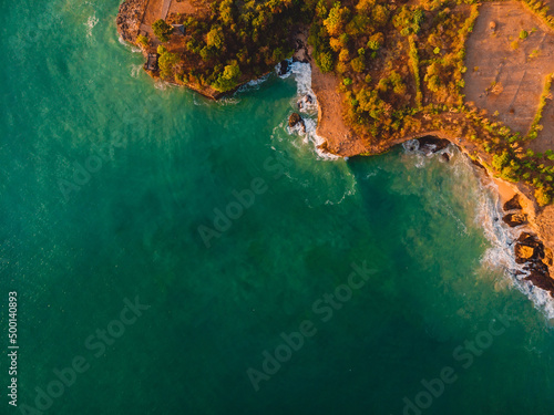 Aerial view of rocky shore with sea and warm light at sunset.