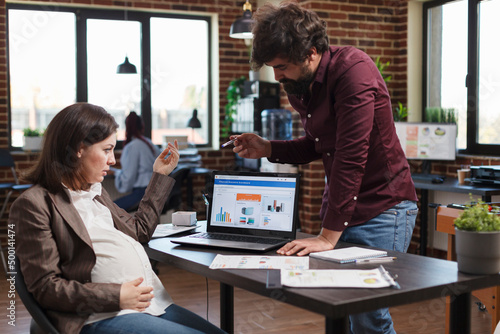 Pregnant woman questioning data charts and business analytics results while sitting at office desk. Financial agency office worker informing finance department manager about poor project strategy.