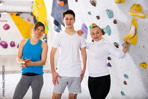 Group photo of women and young man standing in bouldering gym at climbing wall.