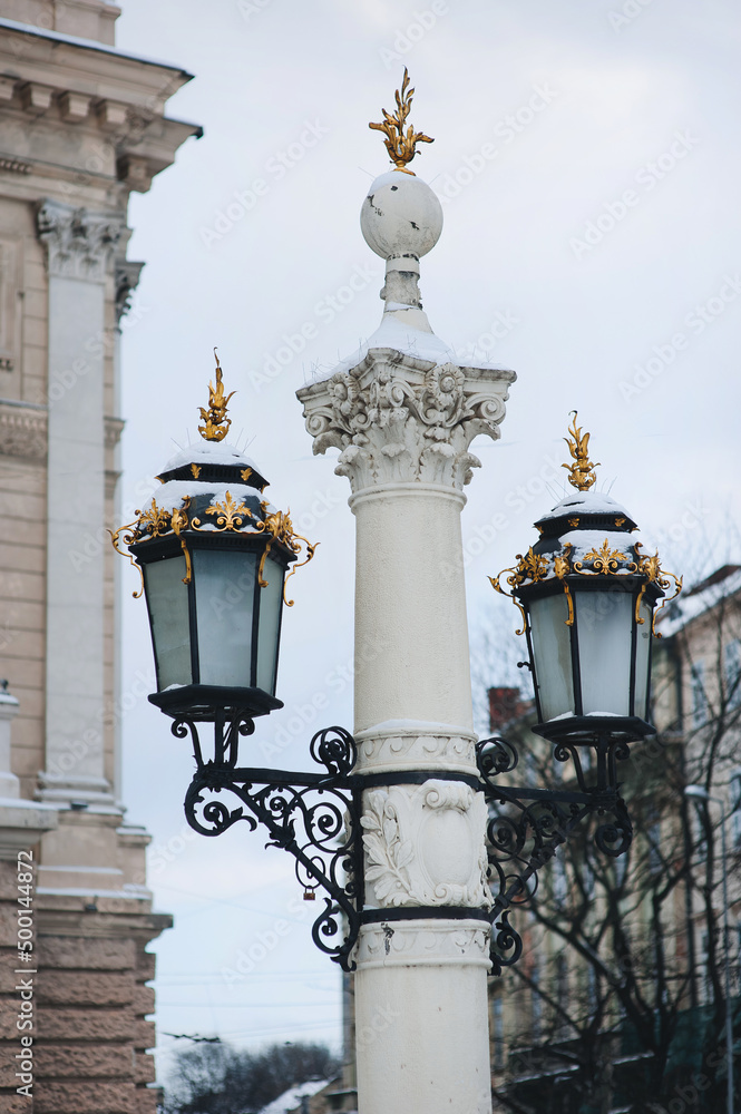 A large old lantern on a thick column with a capital and gilded tops in the historical center of Lviv, near the Opera and Ballet Theatre.
