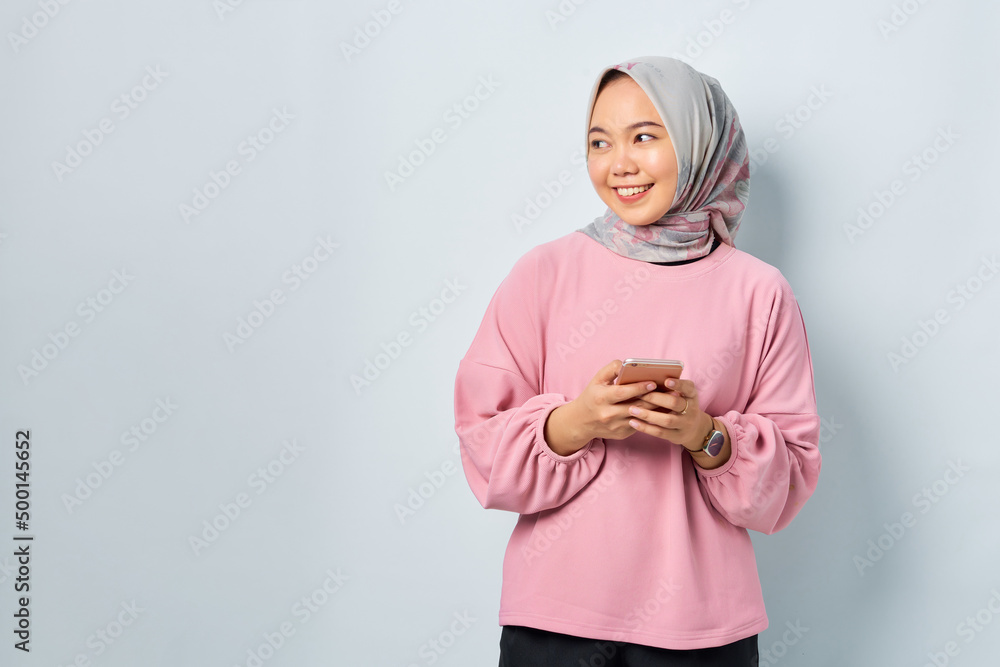 Cheerful young Asian woman in pink shirt using mobile phone and looking away at blank space isolated over white background Cheerful young Asian woman in pink shirt using mobile phone and looking away at blank space isolated over white background