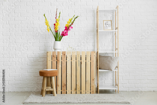 Chair and vase with beautiful gladiolus flowers near white brick wall