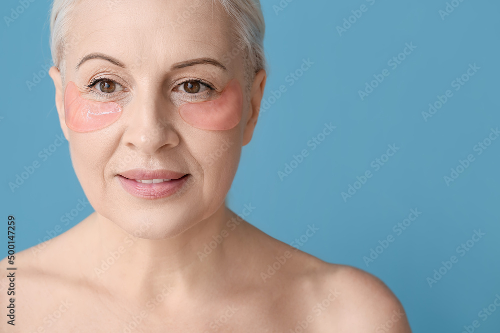 Mature woman with under-eye patches on blue background, closeup