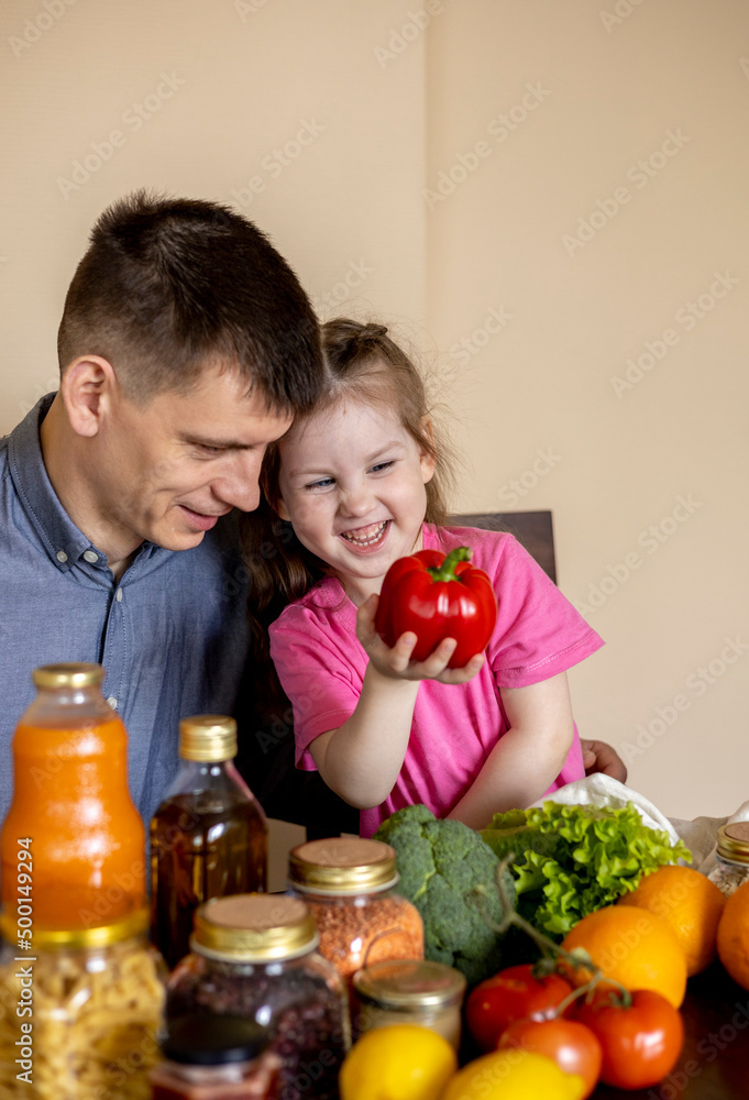 Father and daughter are sitting at the table in the kitchen. Fresh products bought in the store. Father and daughter are sitting at the table in the kitchen. Fresh products bought in the store.