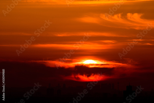 Sunset over the city. Orange sky and sun behind the clouds.