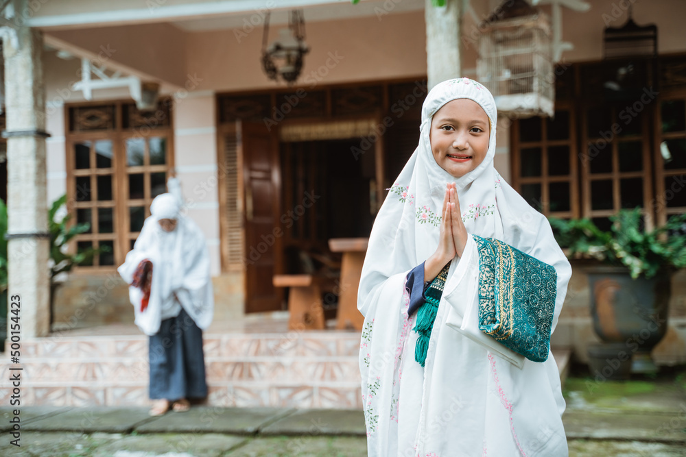 young muslim girl with hijab smiling and greeting to camera with mother in the background