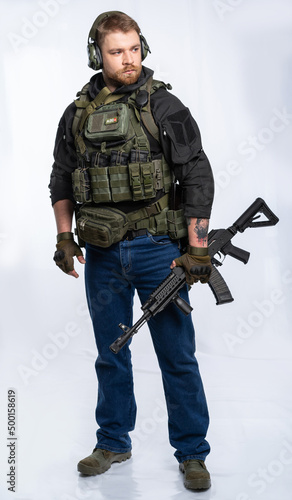 airsoft player in full gear is ready to play. a man in an outfit, in headphones, a bulletproof vest, with a backpack and a belt with additional shells. on a white background.