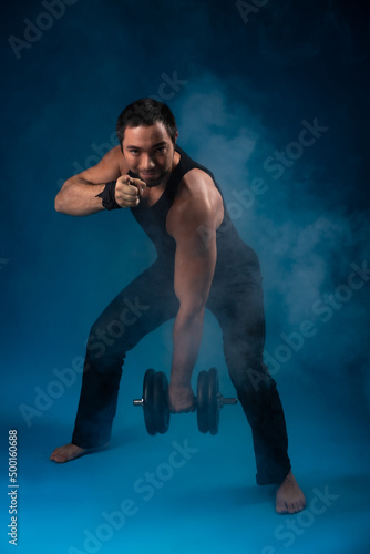 muscular man with dumbbells. sportsman posing in black t-shirt, jeans with dumbbells. studio portrait. blue background