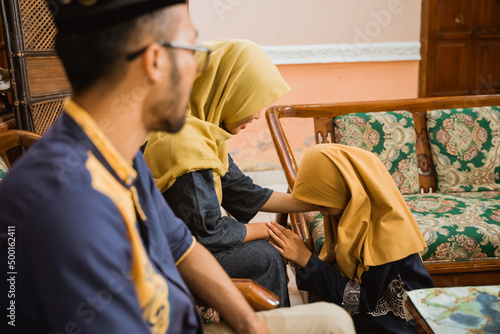 muslim kneeling during eid mubarak. parent give their blessing. family forgiving each other and shake their hand on idul fitri