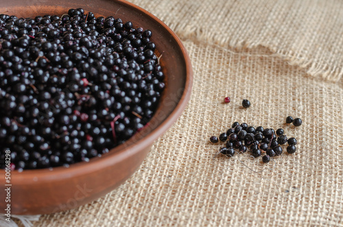 Ripe black elderberries in a brown bowl. Clay bowl on top of the burlap. Sambucus nigra.