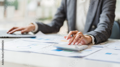 Close up woman hands using calculator and laptop at desk in modern office, accountant and tax concept.