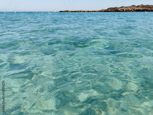Fig Tree Bay beach, crystal clear water, white sand at the bottom, small island off the coast.