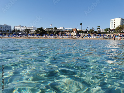 Protaras. Famagusta area. Cyprus. The view from the clearest sea to Fig Tree Bay beach, where people sunbathe and swim, to hotels and restaurants against a cloudless sky.