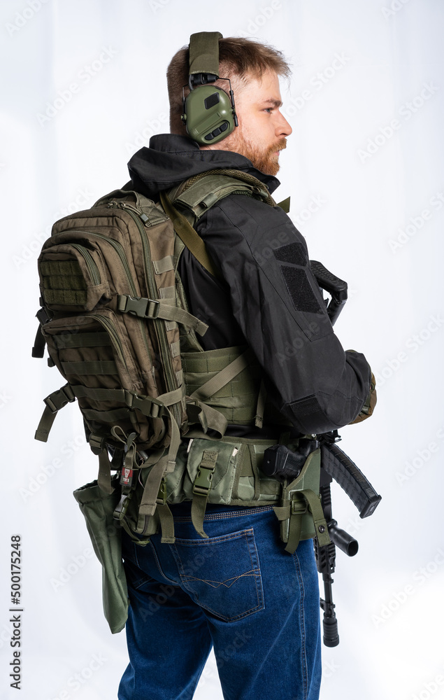 airsoft player in full gear is ready to play. a man in an outfit, in headphones, a bulletproof vest, with a backpack and a belt with additional shells. on a white background. airsoft player in full gear is ready to play. a man in an outfit, in headphones, a bulletproof vest, with a backpack and a belt with additional shells. on a white background.