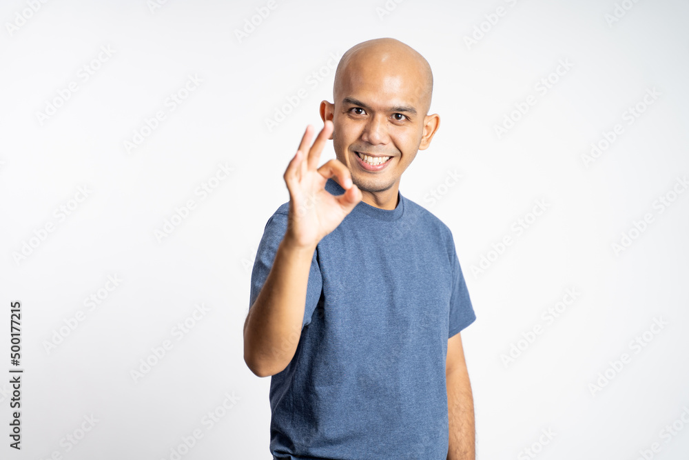 asian bald man smiling with okay gesture while standing on isolated background asian bald man smiling with okay gesture while standing on isolated background