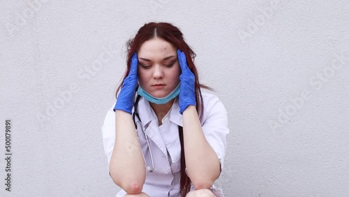 Slow motion footage. Nurse worker have headache migraine feel bad pain tired owerworked after surgery operation. Female doctor dressed medical white gown blue disposable face mask and gloves
 photo