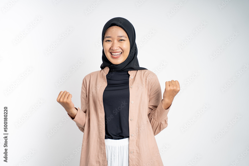 Excited young woman in hijab clenching hands while celebrating success on isolated background Excited young woman in hijab clenching hands while celebrating success on isolated background